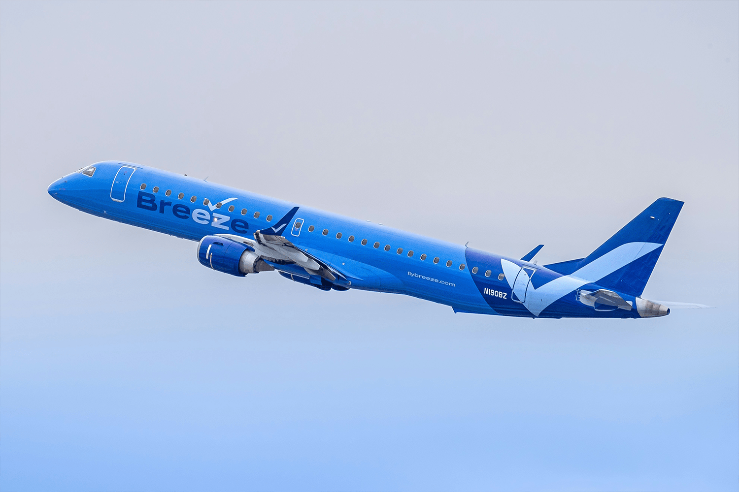 A Breeze Airways commercial aircraft ascending at dusk