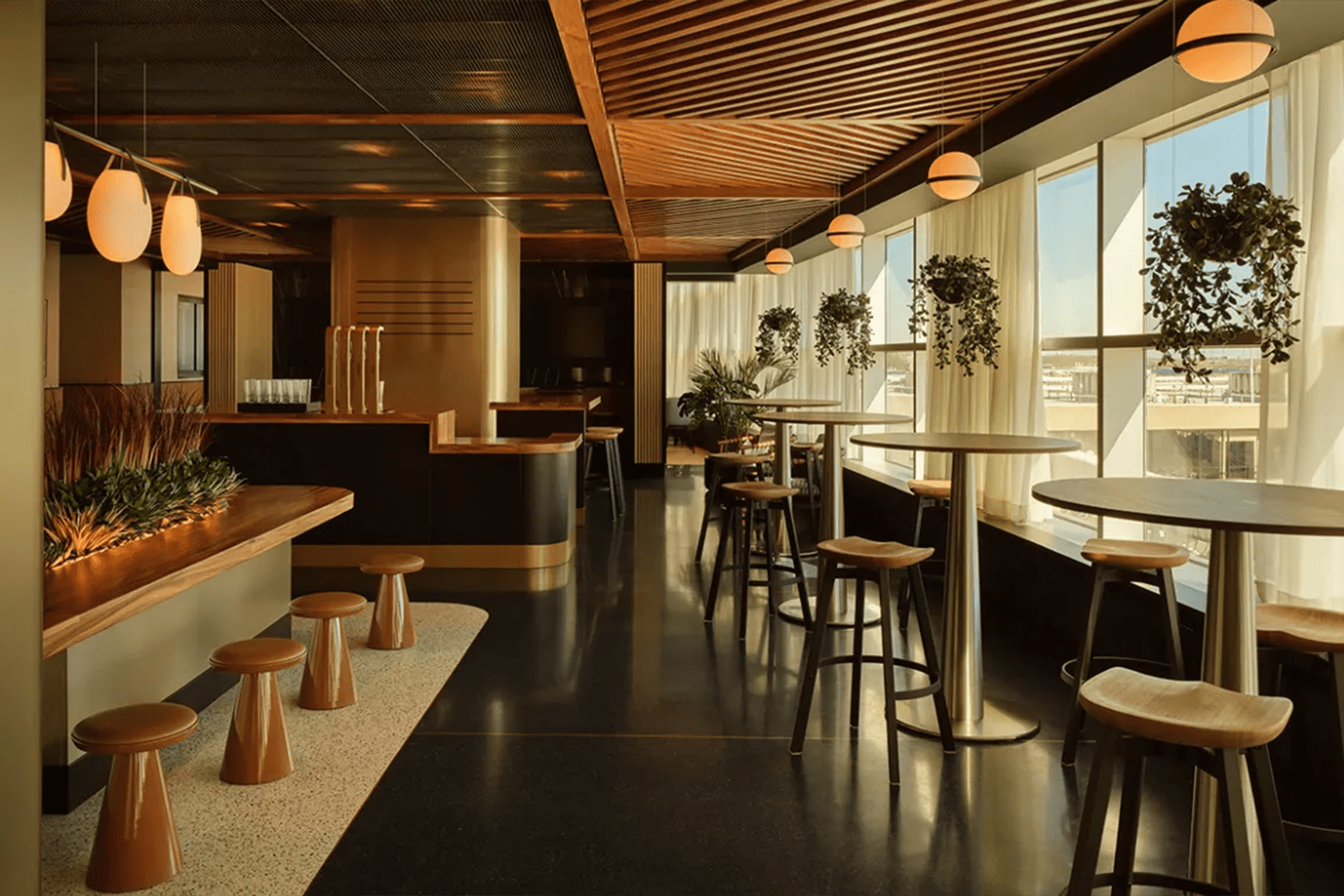Chase Sapphire Lounge at Philadelphia International Airport with warm wood ceilings, hanging plants, high-top tables and stools, a sleek bar area and large windows letting in natural light.