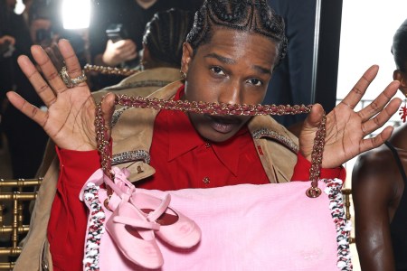 A man holding up a pink bag with baby ballet flats attached to the handle