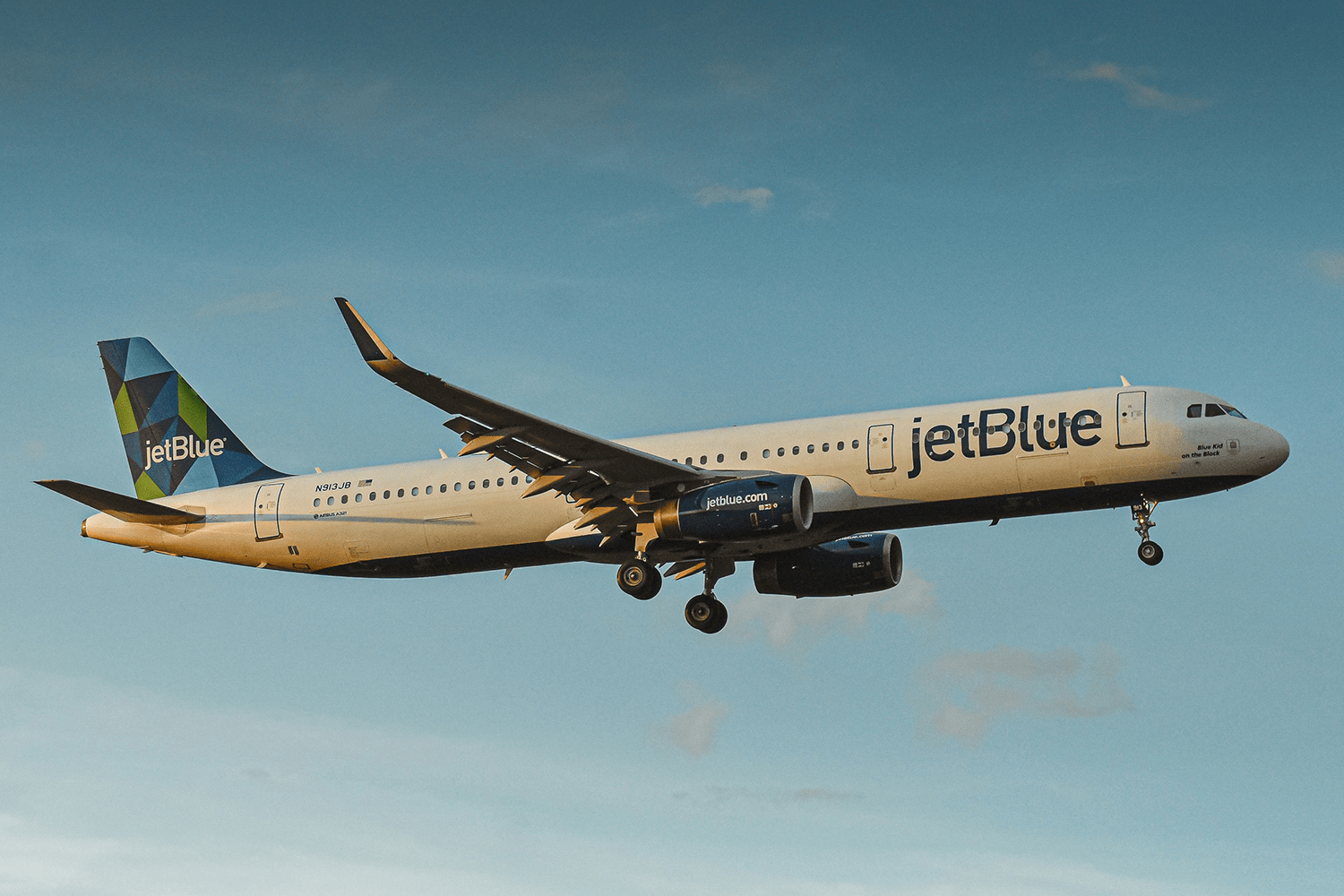 JetBlue airplane flying above a layer of clouds in a clear sky.