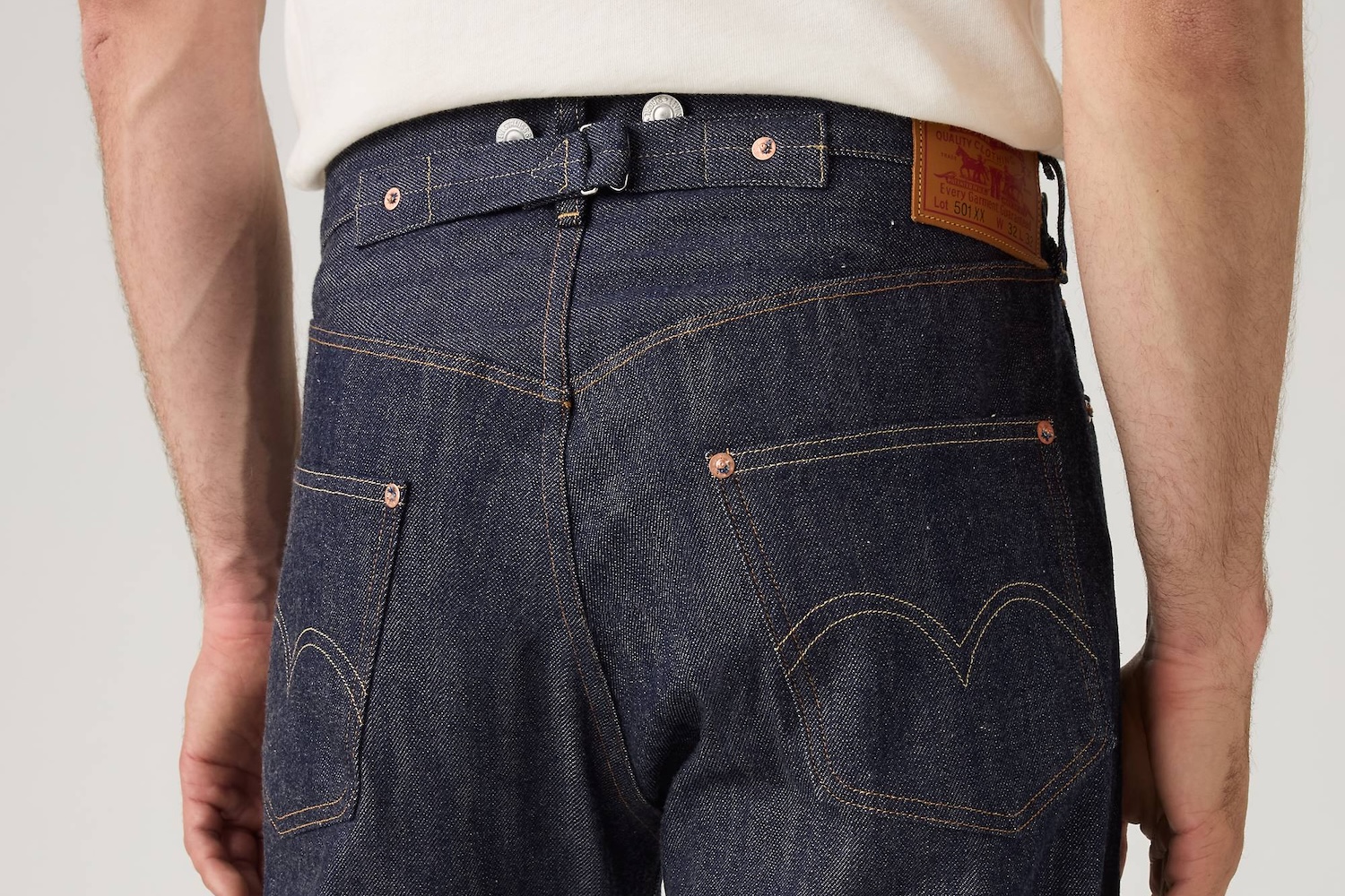 Close-up of the back of a person wearing dark wash denim jeans with a cinch-back, suspender buttons, and a Levi's patch.