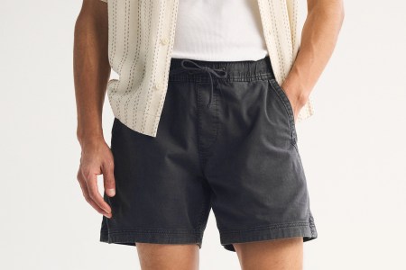 A pair of black shorts on a man, who has one hand in a pocket and one hand out