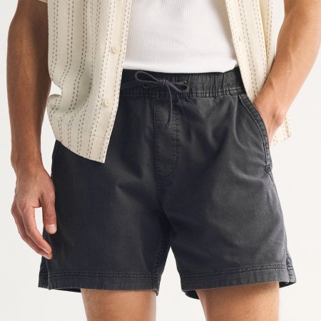 A pair of black shorts on a man, who has one hand in a pocket and one hand out