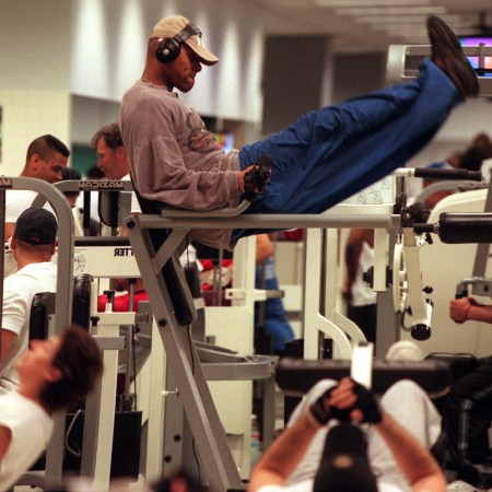 A man wearing headphones and a hat on the captain's chair at the gym surrounded by lots of gym-goers
