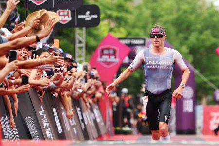 A triathlete wearing sunglasses and a tight shirt and shorts running along a race course and high-fiving people along the way