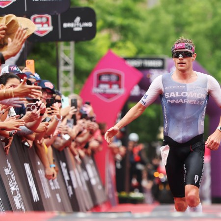 A triathlete wearing sunglasses and a tight shirt and shorts running along a race course and high-fiving people along the way