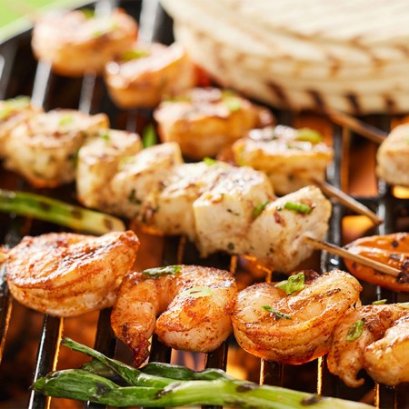 Shrimp and chicken skewers and vegetables on a grill