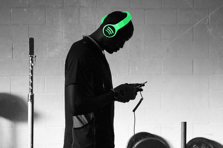 A man looking at a phone, wearing headphones with a lime-green Spotify illustration.