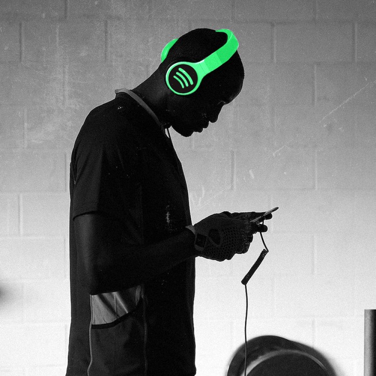 A man looking at a phone, wearing headphones with a lime-green Spotify illustration.
