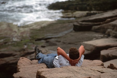 A man laying against the rocks, doing nothing.
