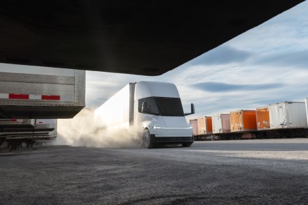 A white semi driving with cargo in the background