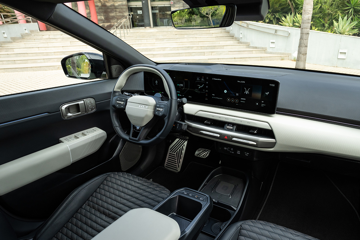 The inside of a car showing the steering wheel, dashboard screen, front two seats and center console