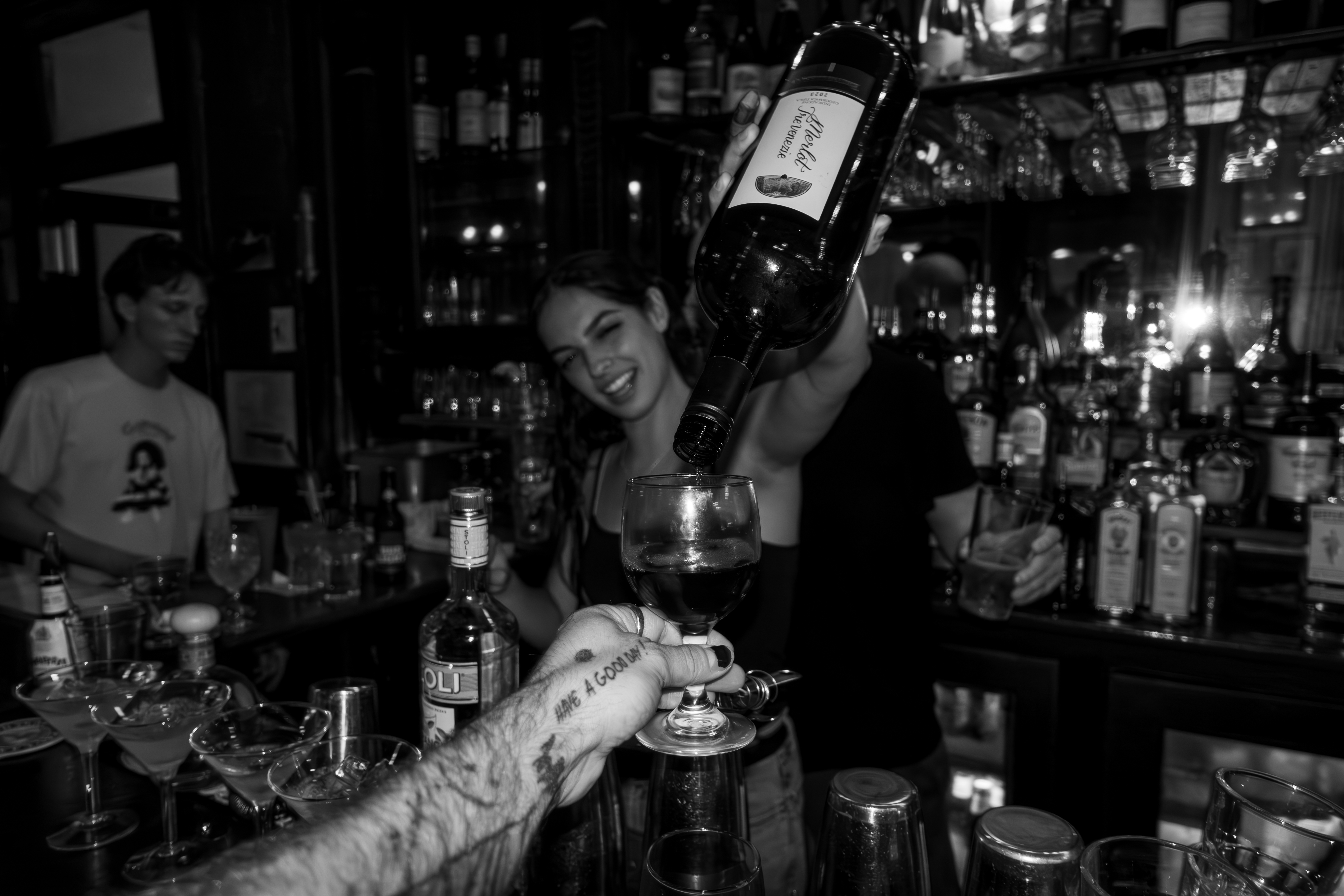 A woman pouring wine behind a bar