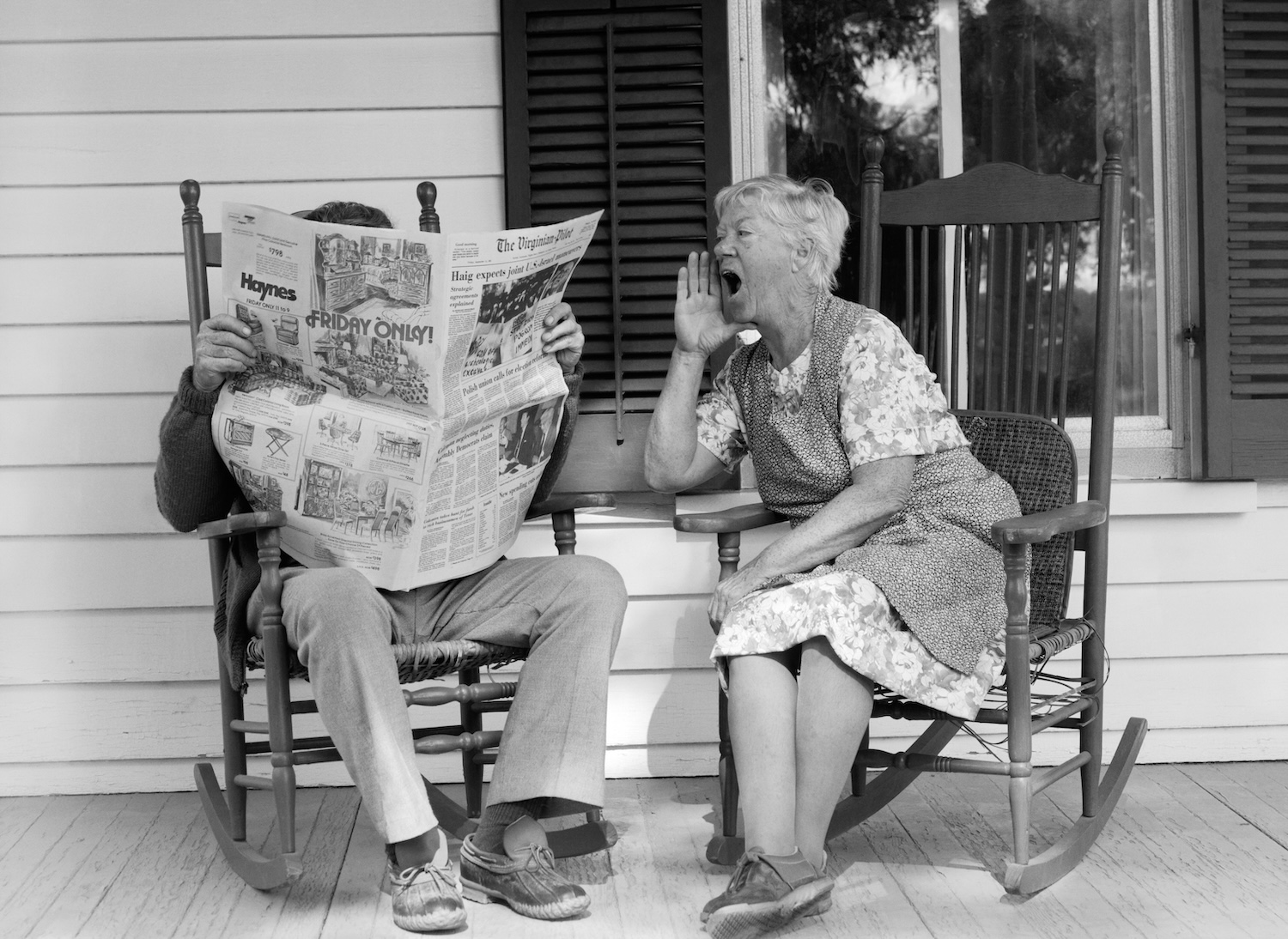 A woman yells at a man reading a newspaper in a chair next to her