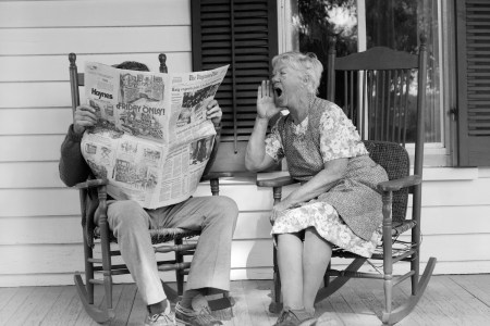 A woman yells at a man reading a newspaper in a chair next to her