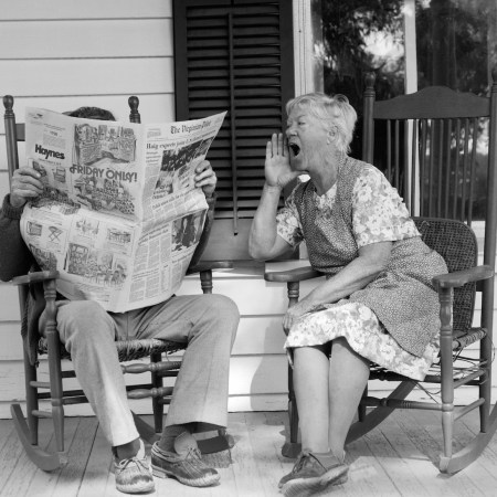 A woman yells at a man reading a newspaper in a chair next to her