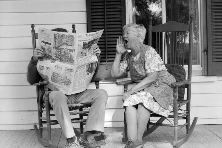 A woman yells at a man reading a newspaper in a chair next to her