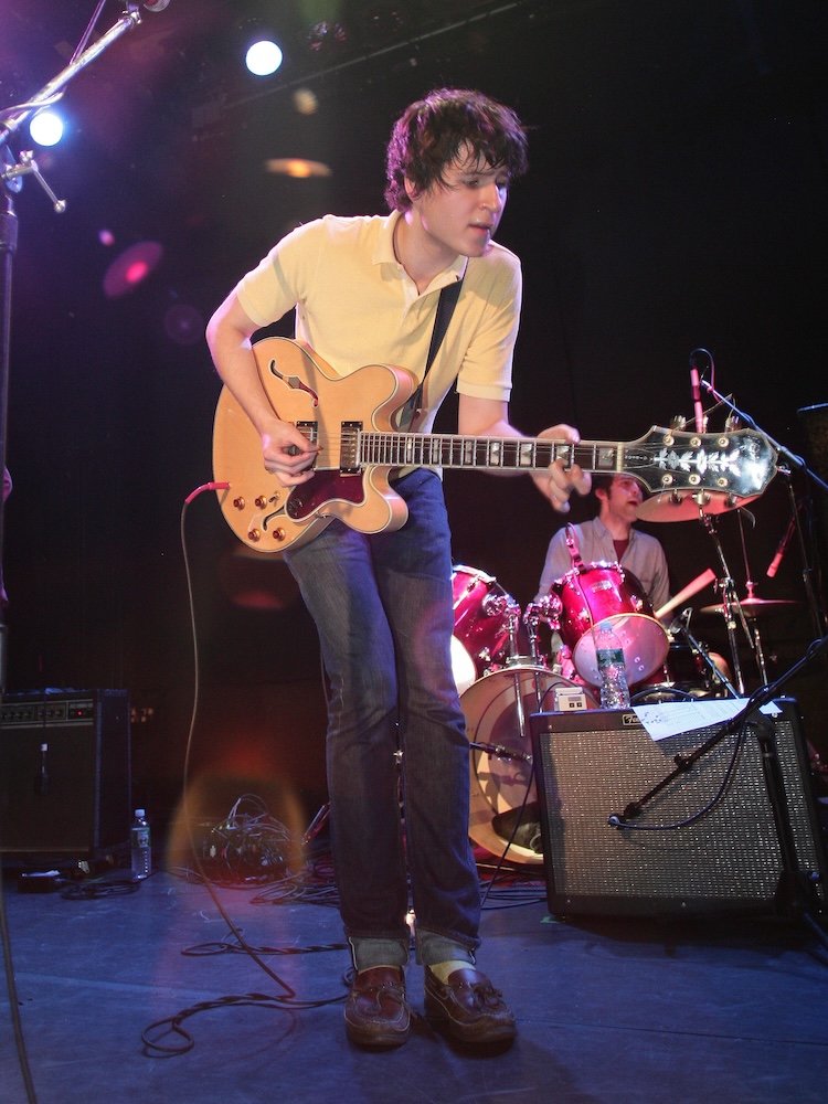 Ezra Koenig wearing a yellow polo and boat shoes.