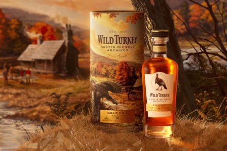 A bottle of whiskey sitting next to a cylindrical container with a barn illustration in the background