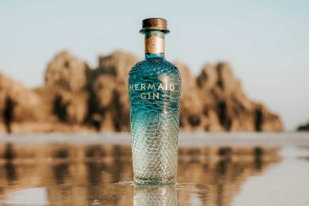 Mermaid Gin bottle on the beach near the ocean water