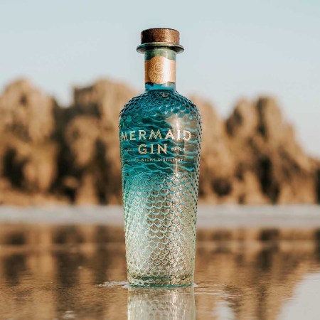 Mermaid Gin bottle on the beach near the ocean water