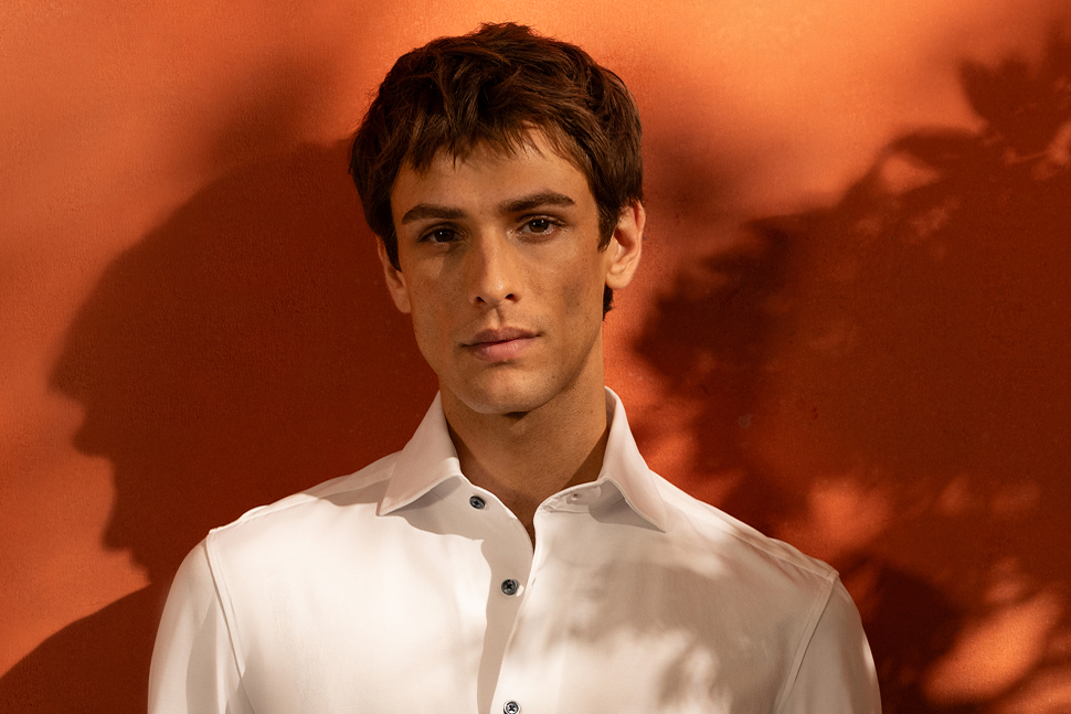 A man in a white shirt standing against an orange wall