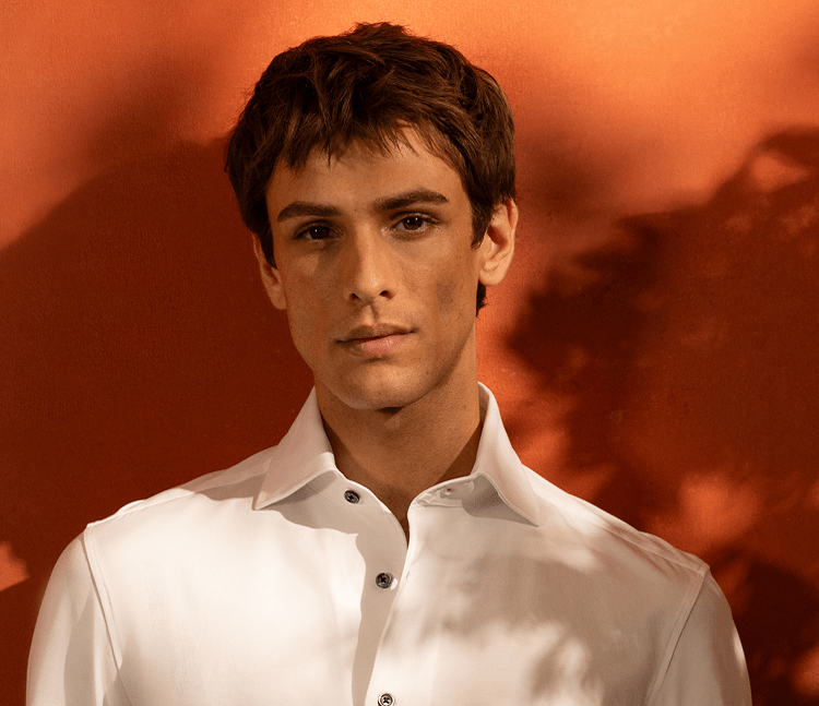 A man in a white shirt standing against an orange wall