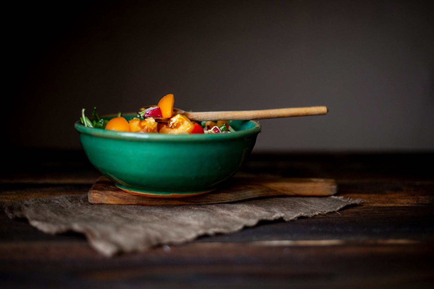 a green bowl filled with tomato salad and a wooden spoot
