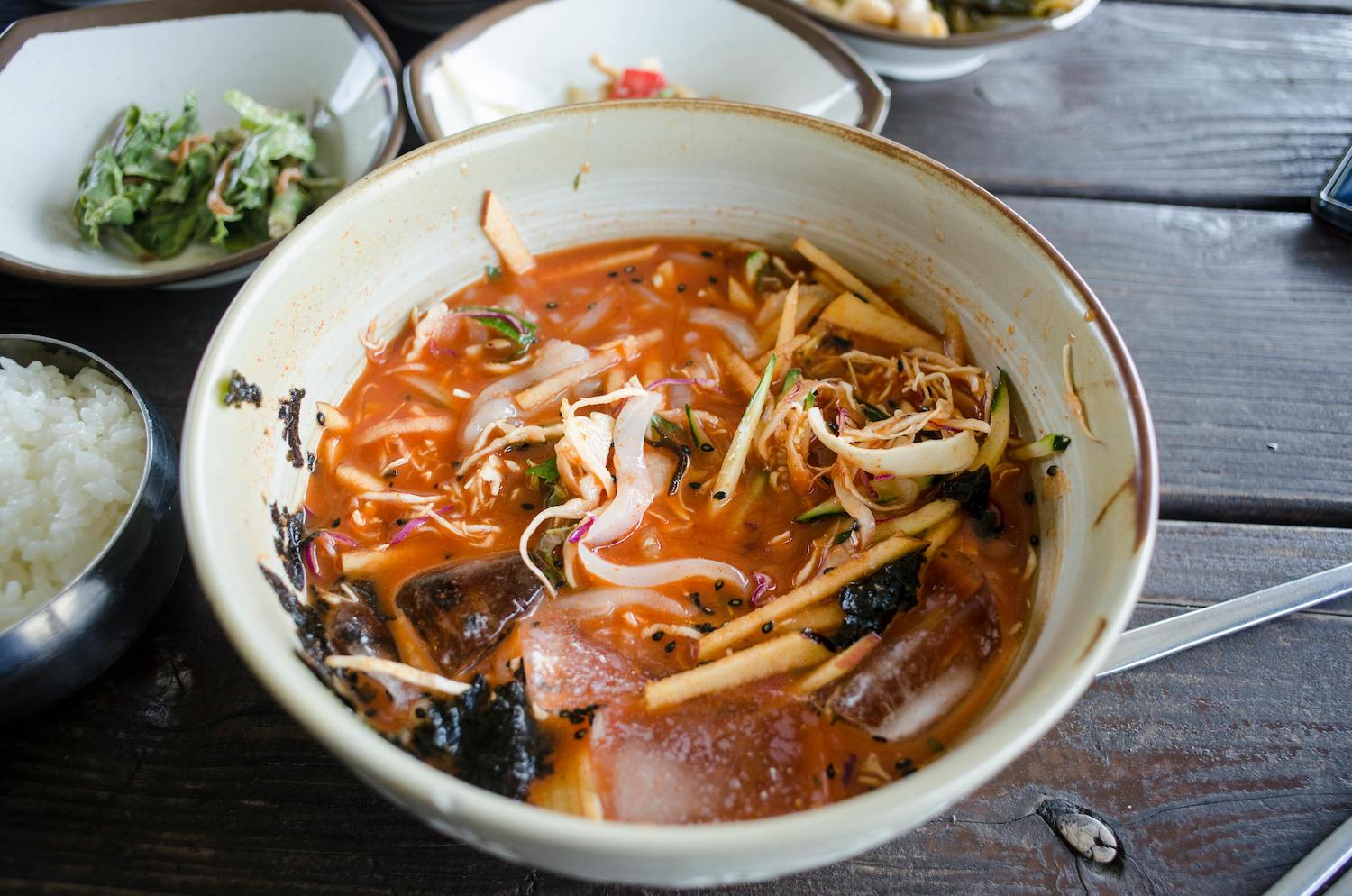 Bowl of Korean noodle soup with spicy broth, vegetables, and seaweed