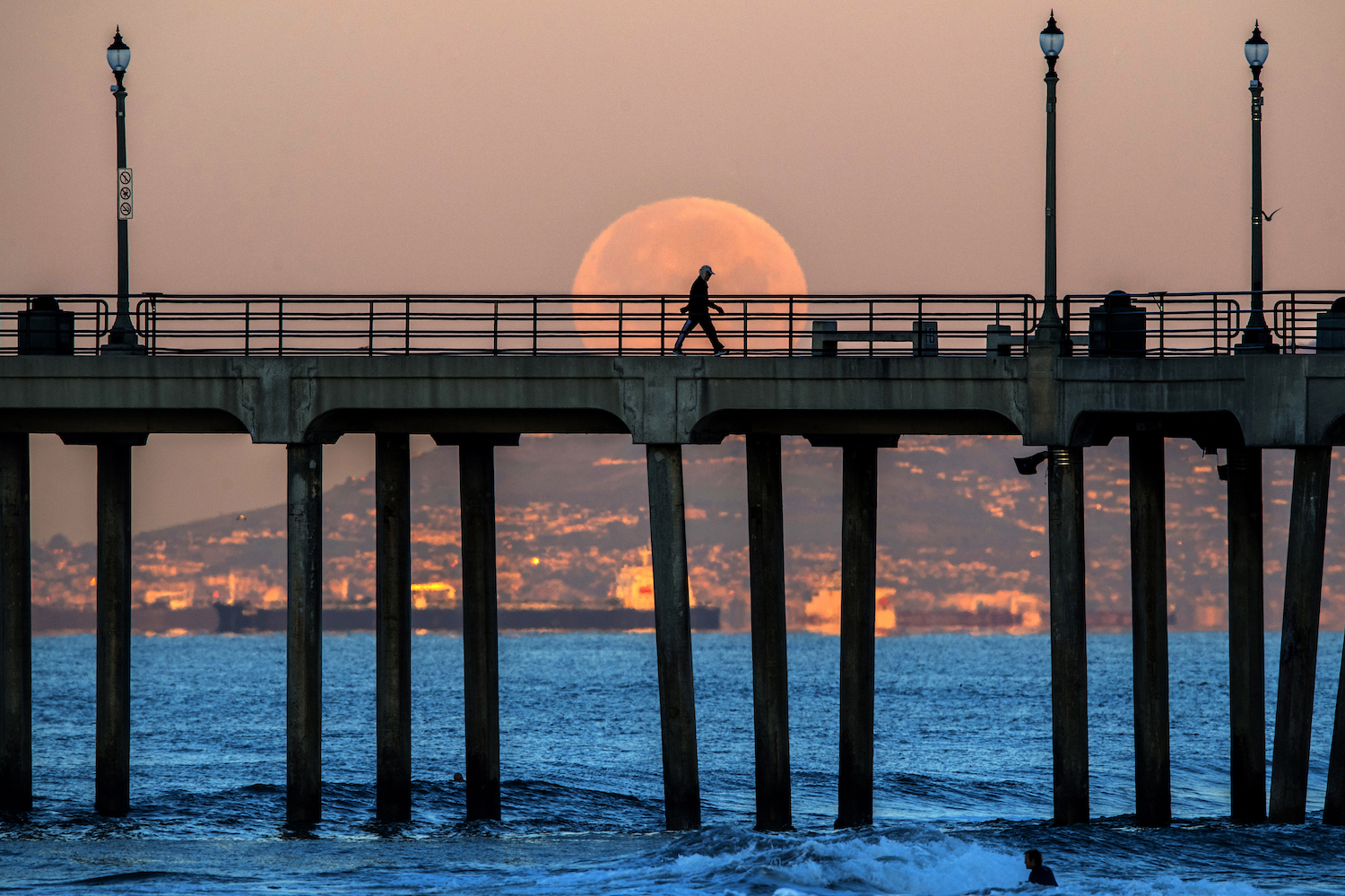 A man walking on a boardwalk in front of a super moon.