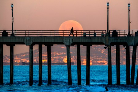 A man walking on a boardwalk in front of a super moon.