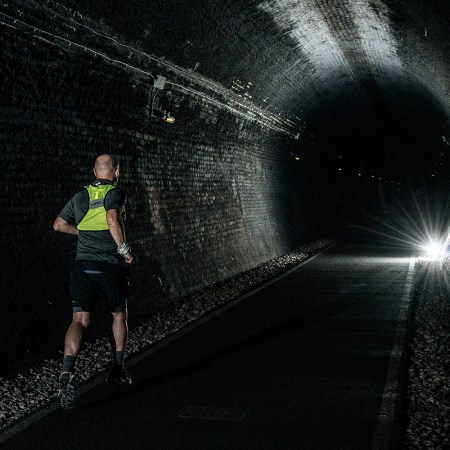 A man running in a high-vis vest through a dark tunnel with a single light shining in the distance