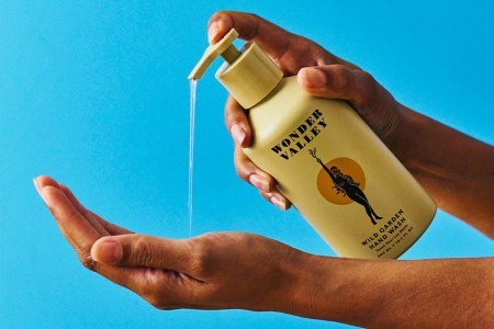 A hand pressing the top of a hand soap bottle with the soap falling onto an open palm with a blue background