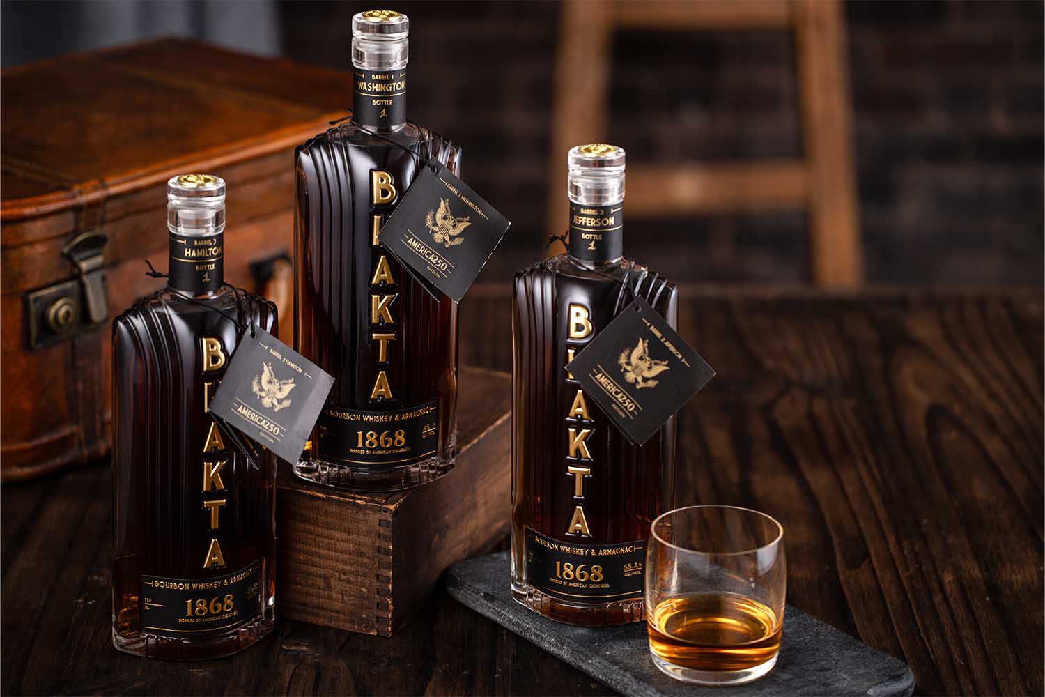 Three bottles of Bhakta 1868 and a glass of whiskey on a table