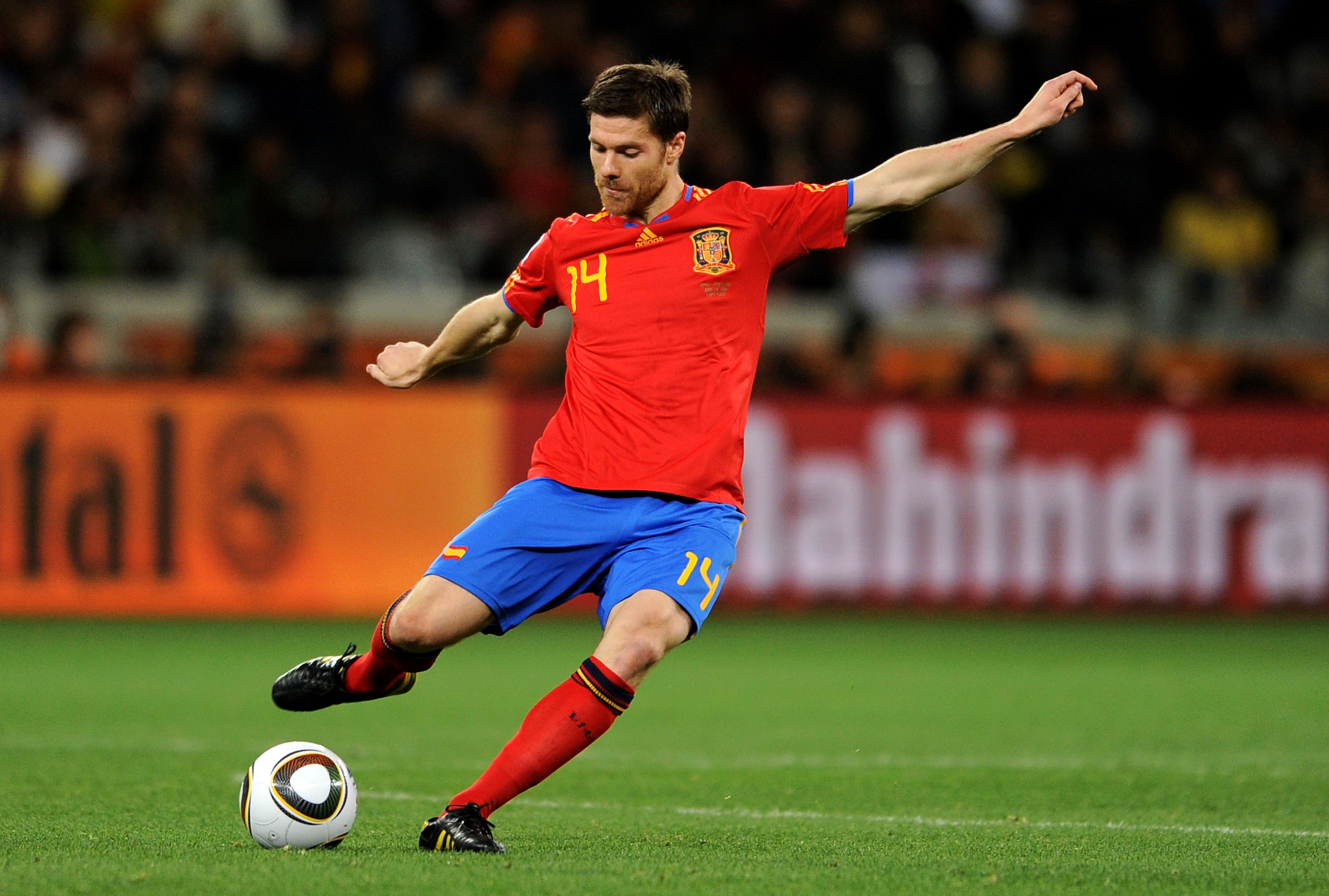 A Spanish player in a red jersey and blue shorts kicking a soccer ball on the field during the World Cup