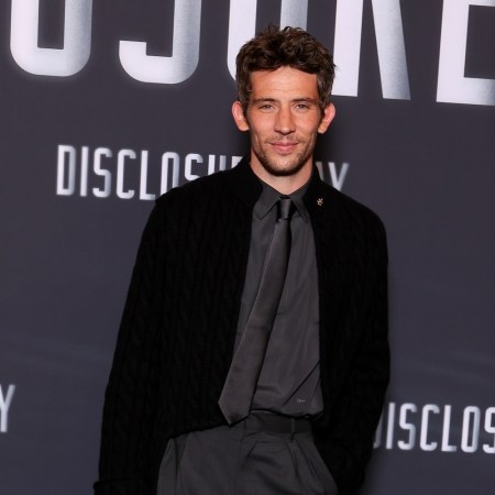 A man in a black cardigan, dress shirt and tie standing in front of a "Disclosure Day" backdrop