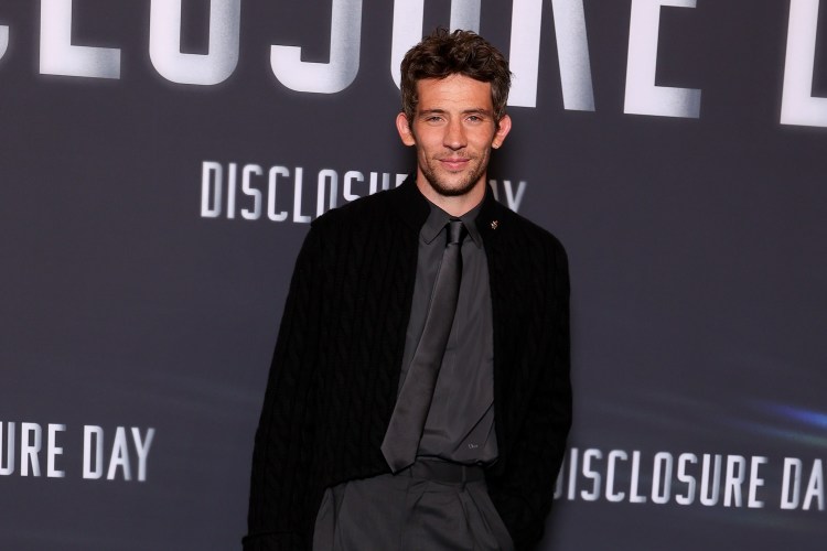 A man in a black cardigan, dress shirt and tie standing in front of a "Disclosure Day" backdrop
