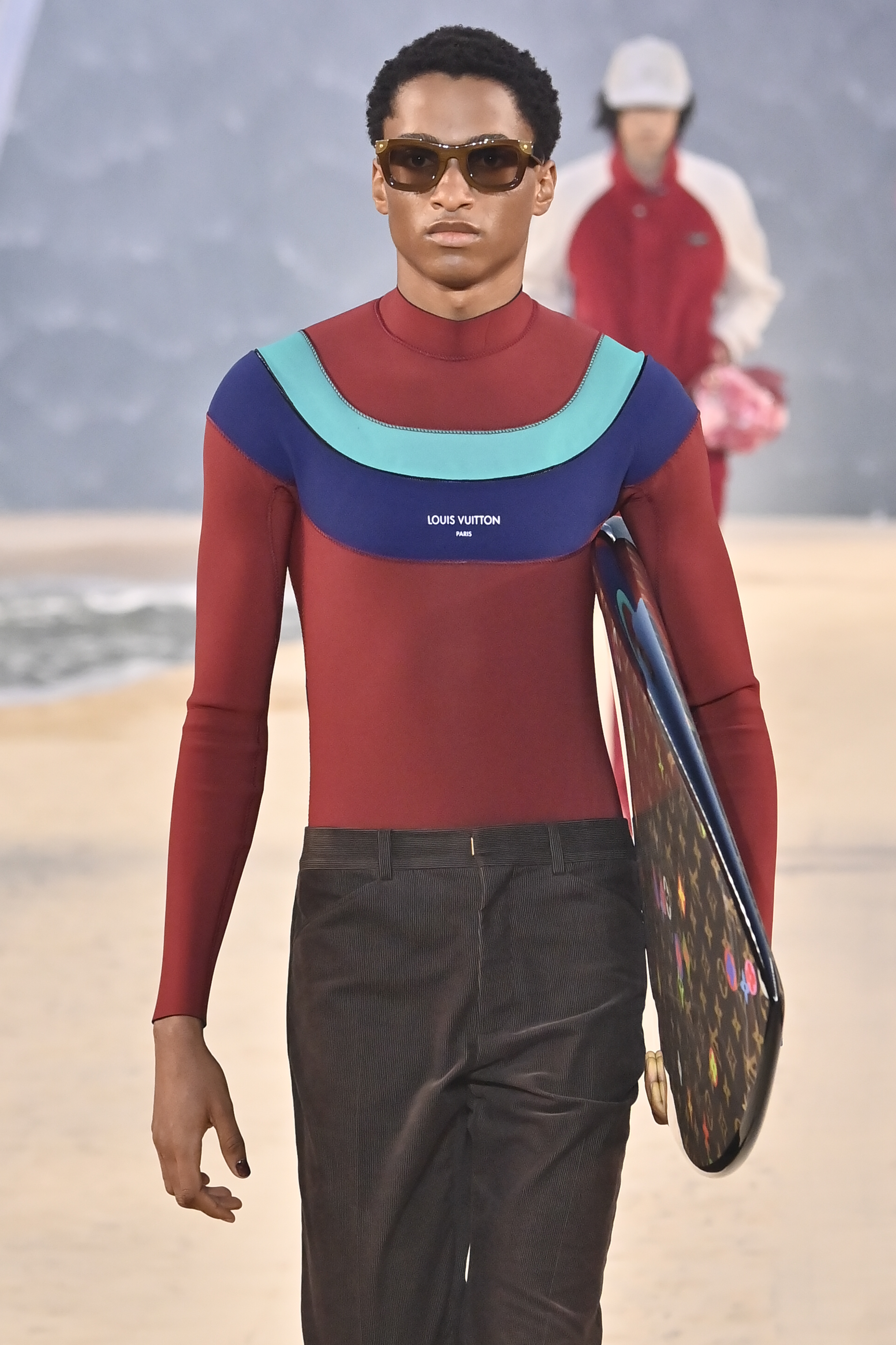 A model holding a surf board walks the runway during the Louis Vuitton Menswear Spring/Summer 2027 fashion show