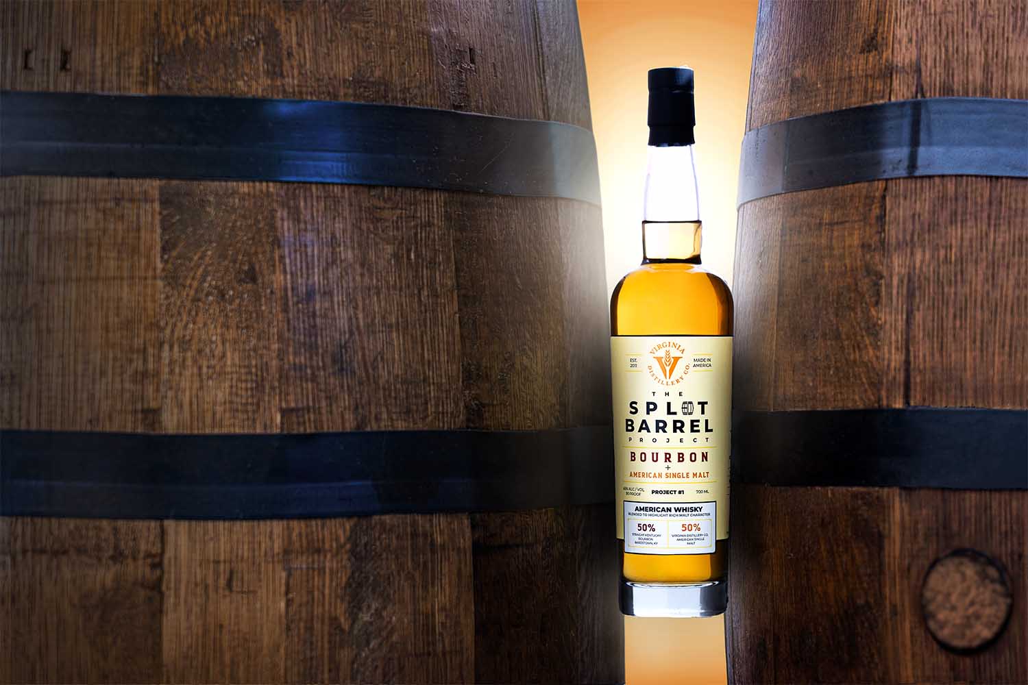 A bottle of VDC Split Barrel between two whiskey barrels