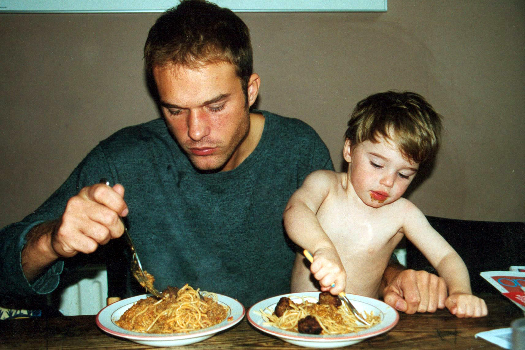 a father and small son eating bowls of spaghetti and meatballs at a wooden table