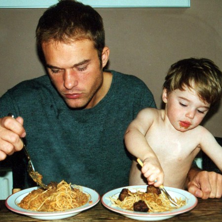 a father and small son eating bowls of spaghetti and meatballs at a wooden table