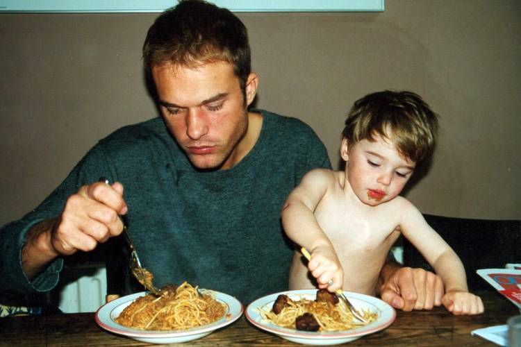 a father and small son eating bowls of spaghetti and meatballs at a wooden table