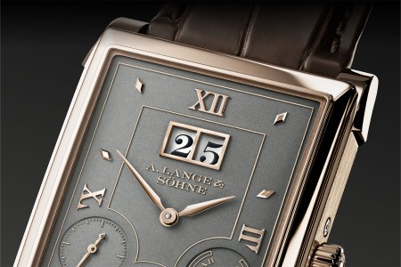 A close-up view of a watch dial with a golden bezel, grey dial and calendar windows with the numbers 25