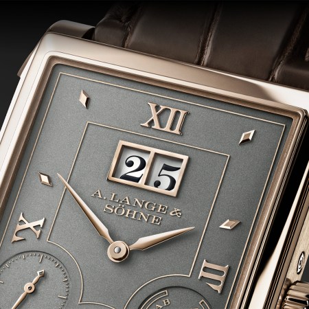 A close-up view of a watch dial with a golden bezel, grey dial and calendar windows with the numbers 25