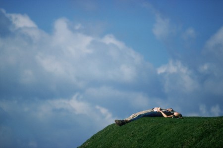 A couple resting on a hill under the sky.