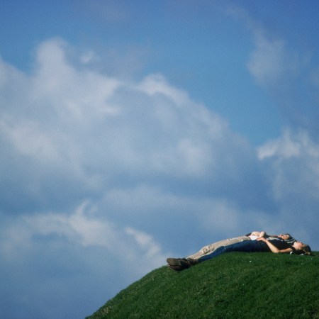 A couple resting on a hill under the sky.