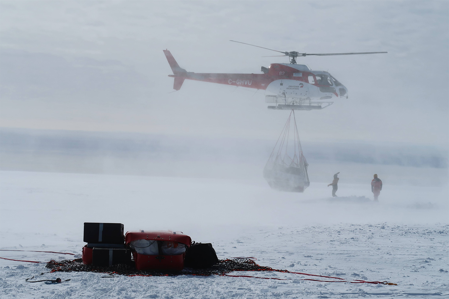 A helicopter carrying a sling of supplies onto the Canisteo Peninsula in Antarctica with more supplies in the foreground