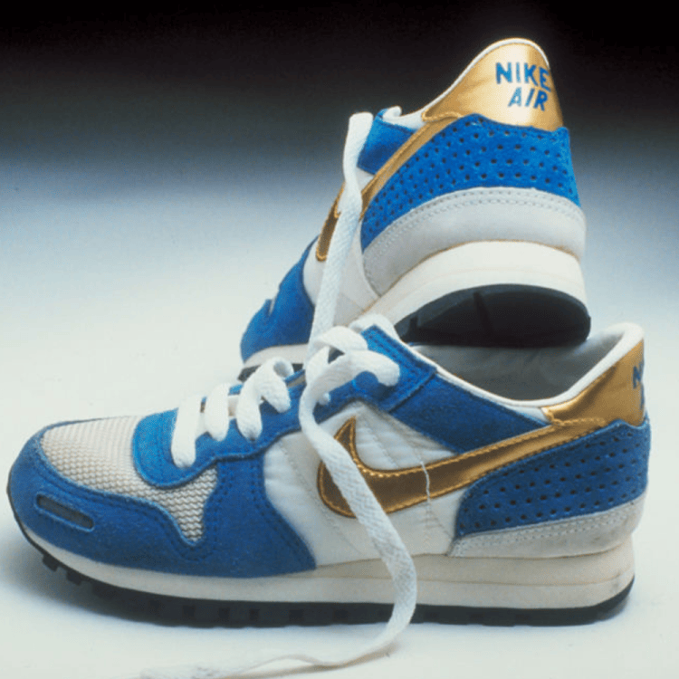 Pair of vintage Nike Air sneakers in blue, white, and gold, one standing upright behind the other.
