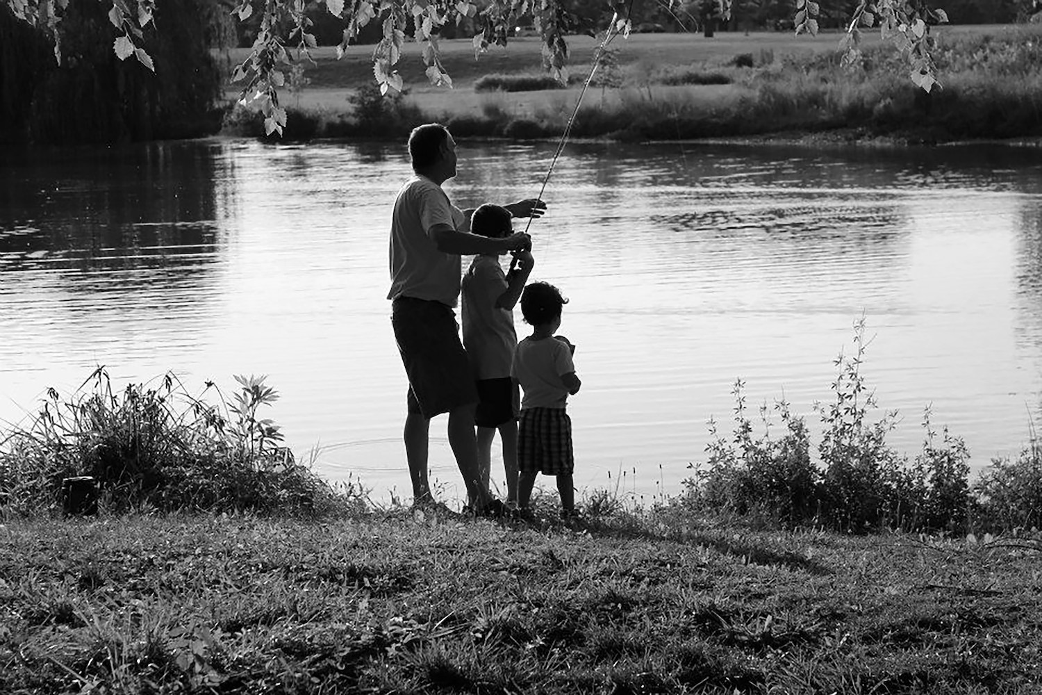 a black and white photo of a man and two children by a river