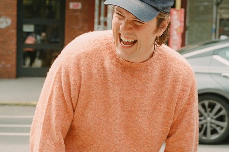 A man in a peach sweater with a New York Rangers baseball cap laughing, with the text "What's in Your Algo?" over the top
